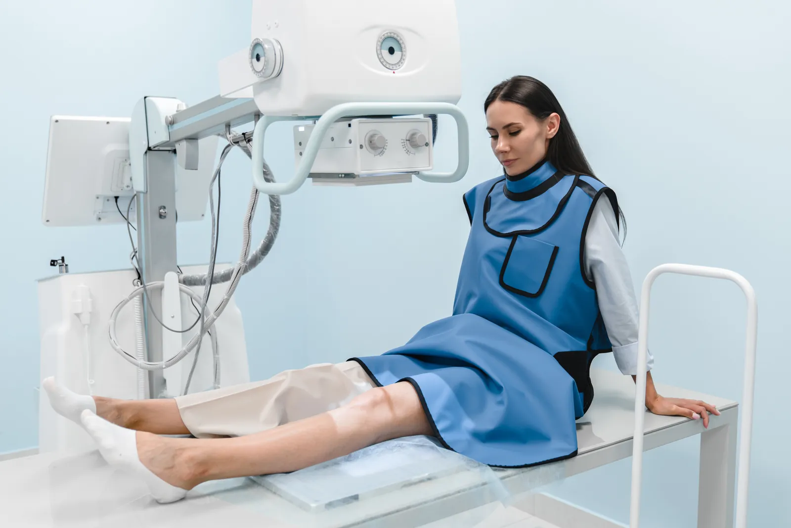 Woman in a protective lead apron sits on a treatment couch with her knee positioned under an imaging machine